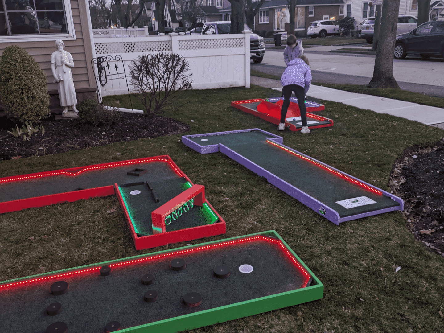 A portable LED mini golf course laid out on grass. Two children are playing on the boards towards the far right of the image. 