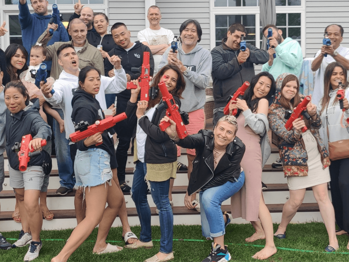 a group of adult laser tag players posing on a backyard deck. adults have a combination of blue and red laser tag blasters held in their hands.