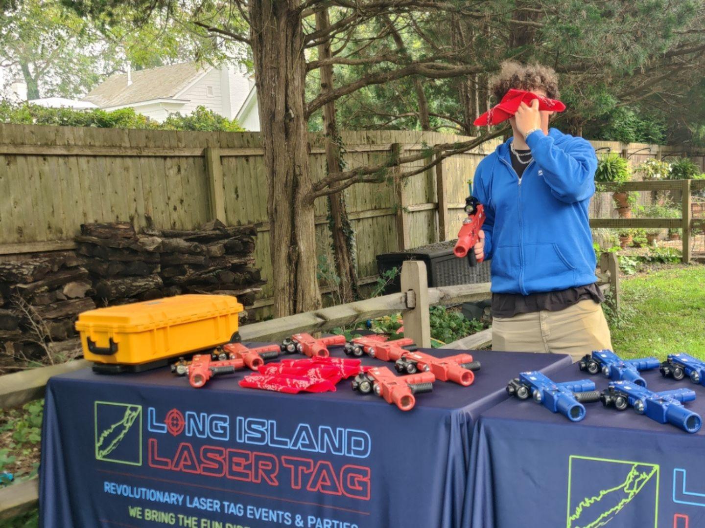 a long island laser tag employee holding a bandana over his eyes. he is also holding a laser blaster with his right hand. 
