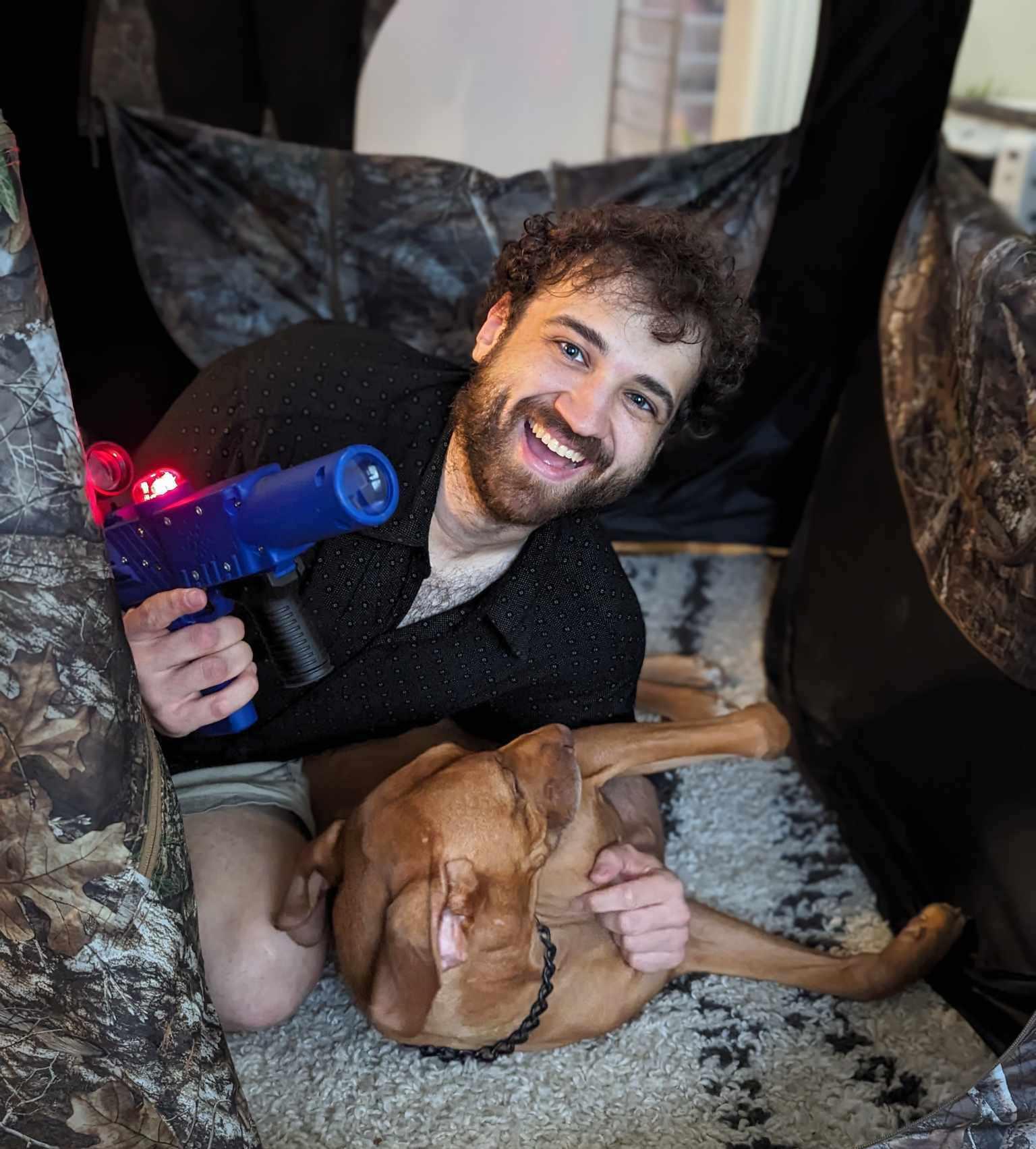 Smiling adult man holding laser tag gun with dog