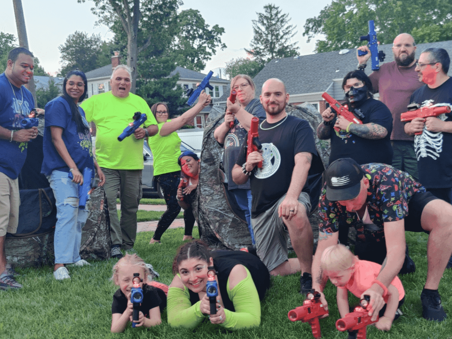 a group of adults holding laser blasters. some are on the red team, some are on the blue team.