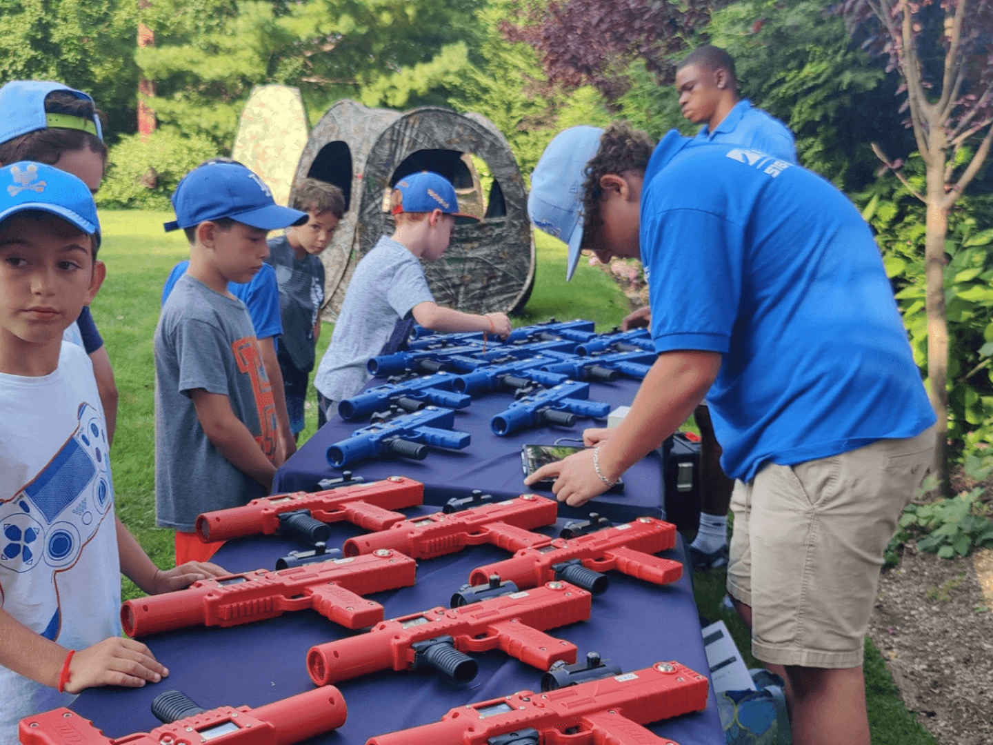 a long island laser tag employee preparing a laser blaster for use. five children are on the left side of the screen, there is a table with blue and red laser taggers separating the children from the laser tag employee on the right. 