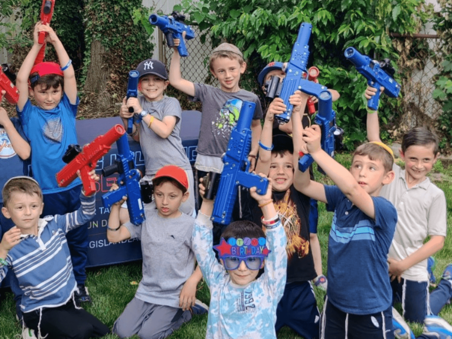 a large group of children raising laser tag blasters in the air in front of a branded table from the company long island laser tag. 